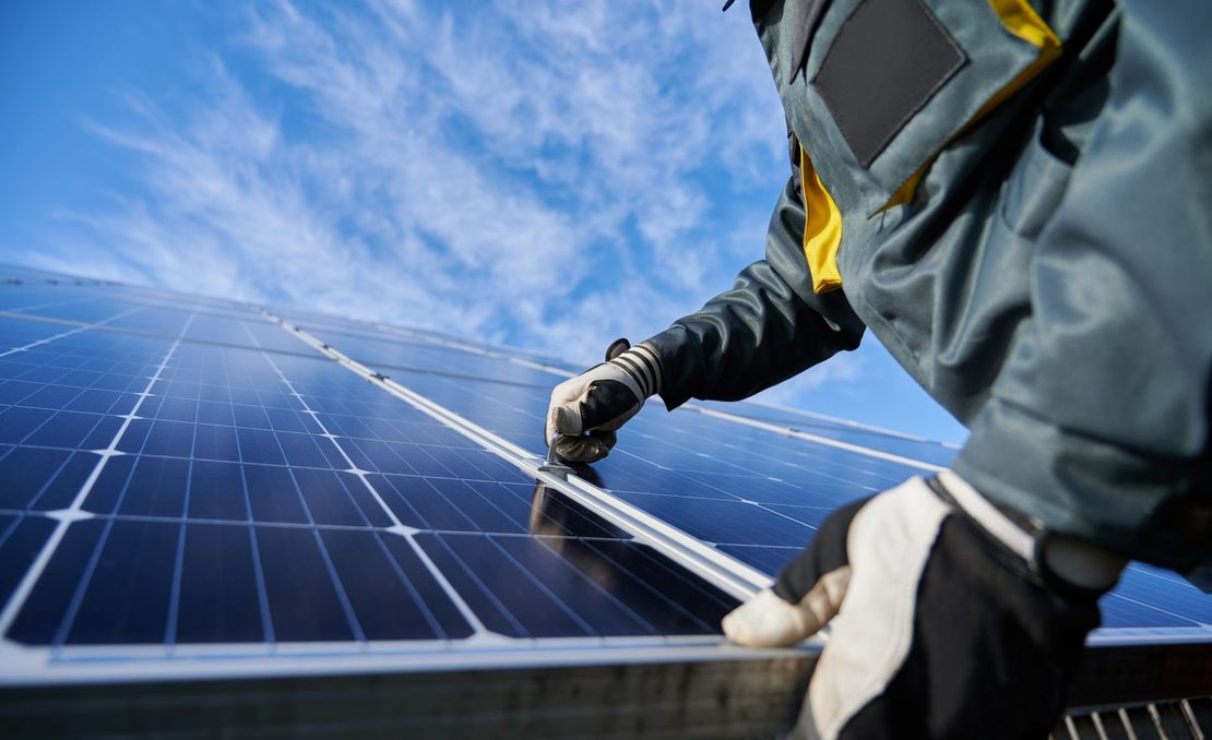 Un technicien nettoie des panneaux solaires sous un ciel bleu.