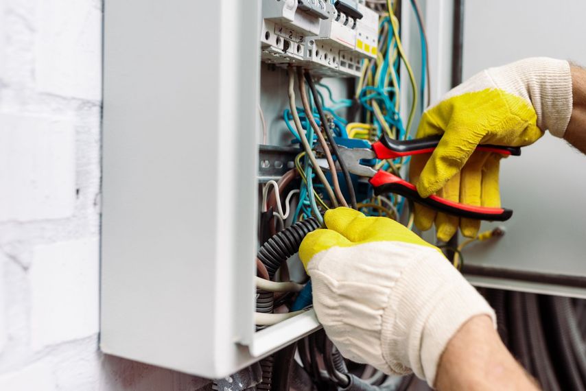Électricien effectuant le câblage d'un tableau électrique ouvert avec des gants isolantsjaunes