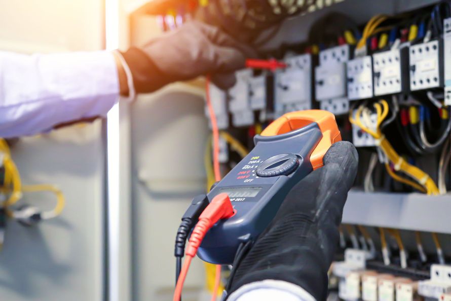 Technicien testant un panneau de commande électrique avec un multimètre et des gants