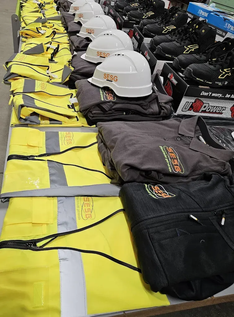 Équipements de sécurité disposés sur des tables : gilets jaunes, casques blancs et vestes de travail noires.