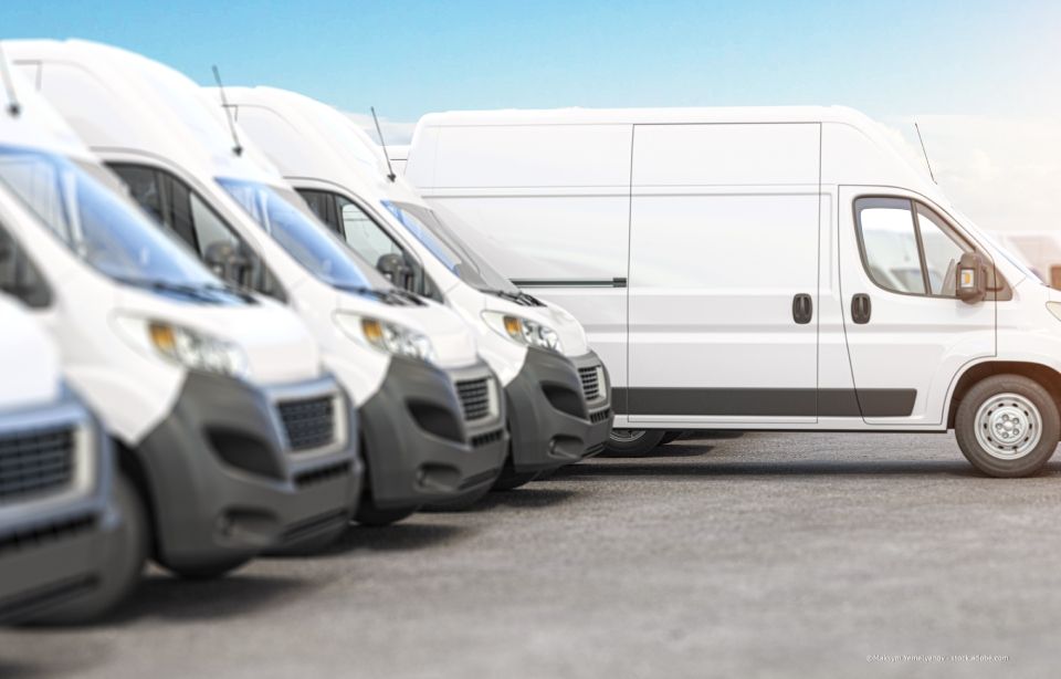 Weisse Transporter, die in einer Reihe auf einem Parkplatz stehen, von vorne links betrachtet.