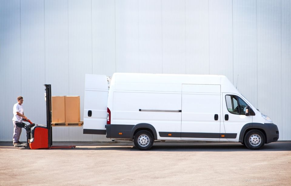 Eine Person lädt mit einem Hubwagen Kartons auf einen weissen Umzugswagen auf einem Industriegelände