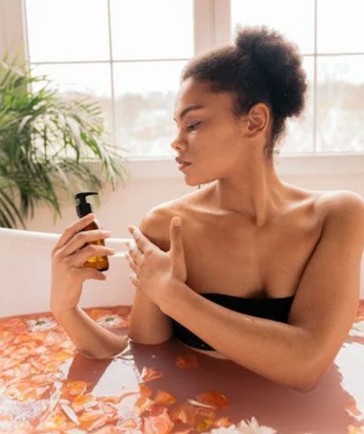 Una mujer está sentada en una bañera sosteniendo una botella de loción.