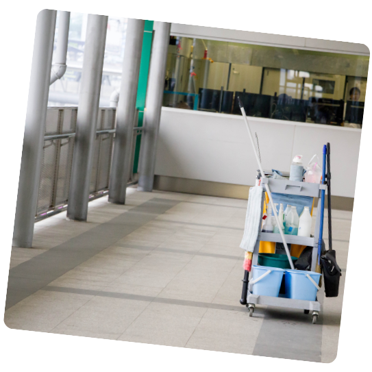 Un chariot de nettoyage rempli de produits est posé sur une allée carrelée, à côté de supports métalliques et d'une vitre.