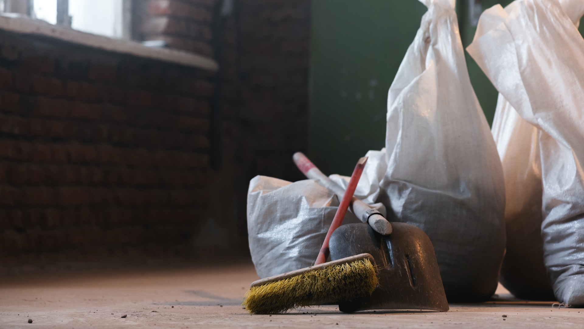 Sacs de débris et de produits de nettoyage sur un sol poussiéreux dans une pièce, fenêtre en arrière-plan.
