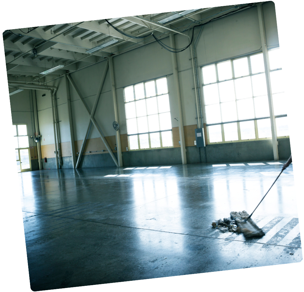 Intérieur d'un entrepôt en cours de nettoyage ; sol brillant, grandes fenêtres, poutres métalliques.