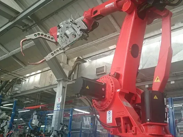 Un brazo robótico rojo está trabajando en una fábrica.