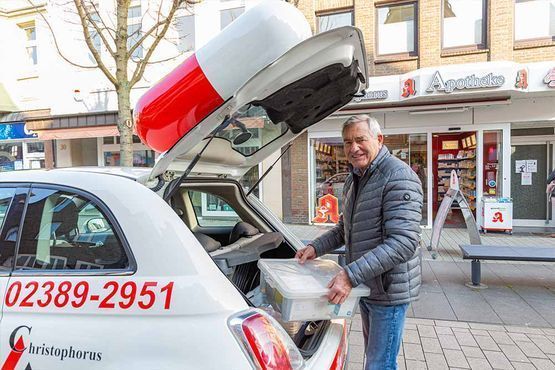 Ein Mann lädt einen Behälter mit Medikamenten in den Kofferraum eines geparkten Autos.