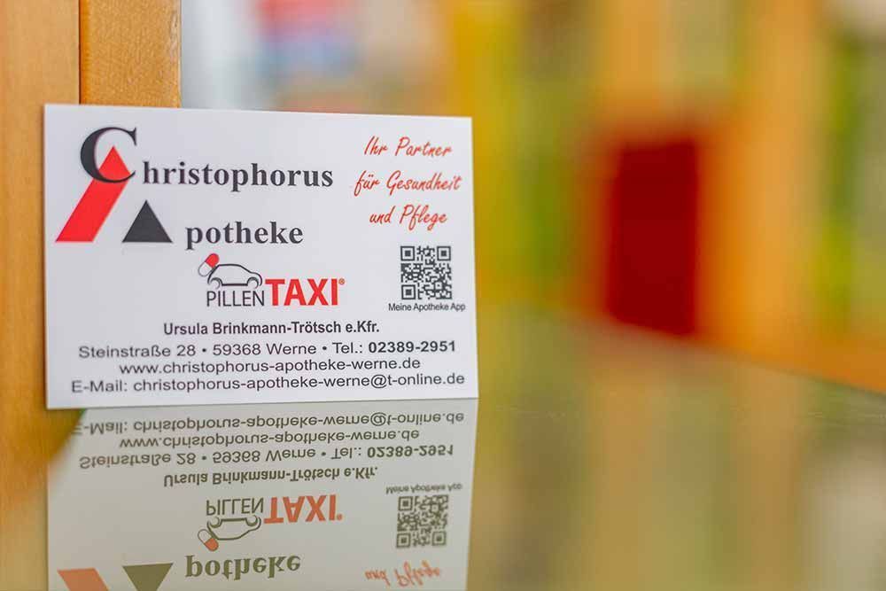 Visitenkarte für Christophorus Apotheke und Pillen TAXI mit Kontaktdaten, dargestellt auf einer reflektierenden Oberfläche.
