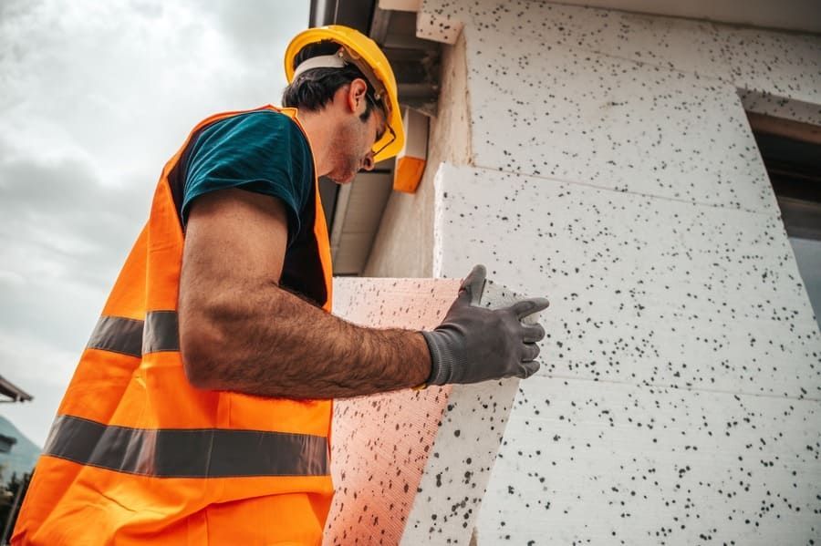 Un trabajador de la construcción está instalando aislamiento en el costado de un edificio.