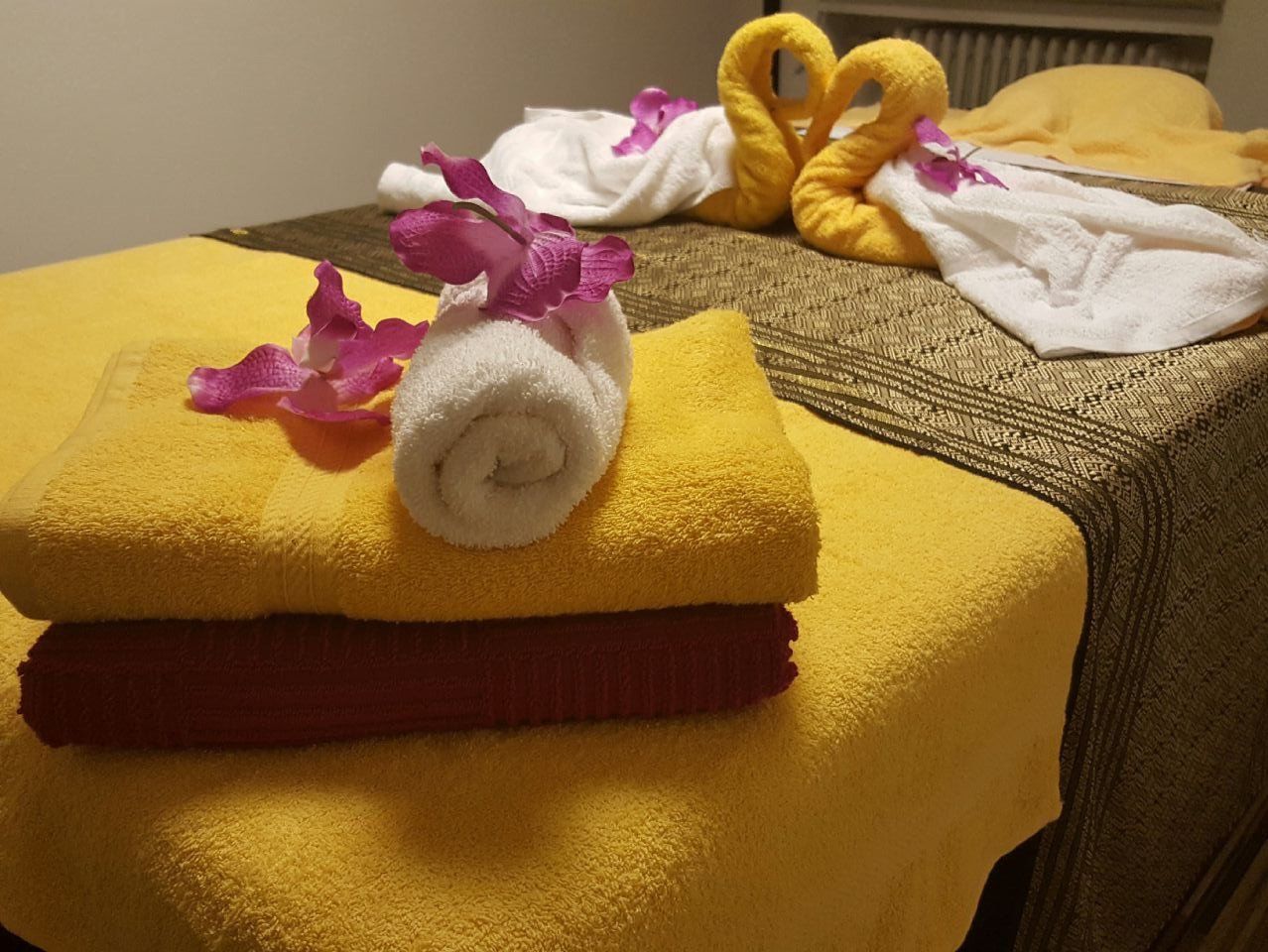 Massageliege mit gelben und weißen Handtüchern mit Orchideenblüten verziert