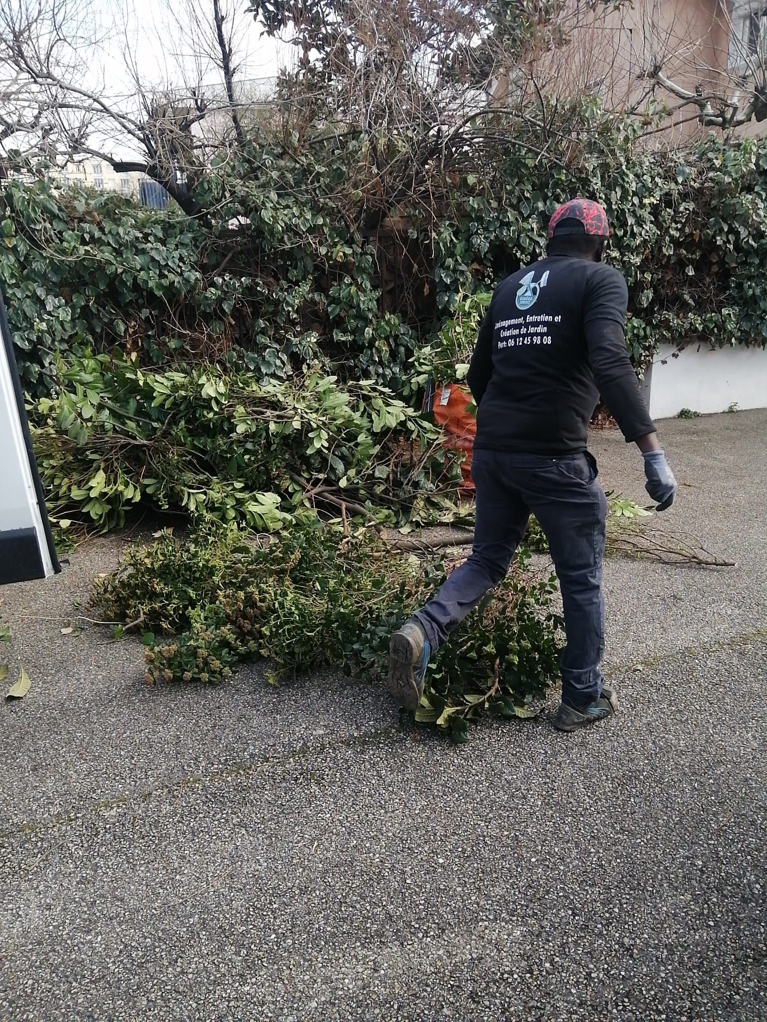 Jardinier proche d'un tas de branches d'arbres posées au sol après des travaux de taille ou d'élagage