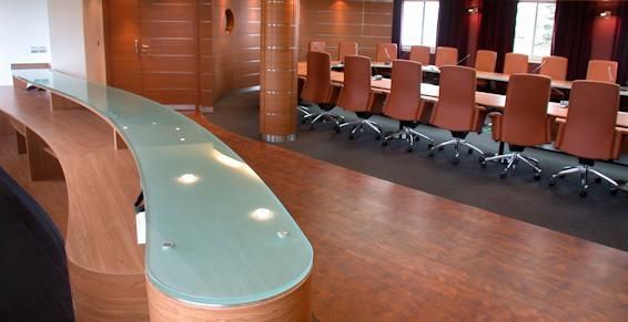 Un bar en bois incurvé avec un comptoir en verre donne sur une longue table de conférence avec des chaises.