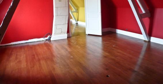 Pièce aux murs rouges, parquet brillant, moulures blanches et porte donnant sur une pièce jaune.