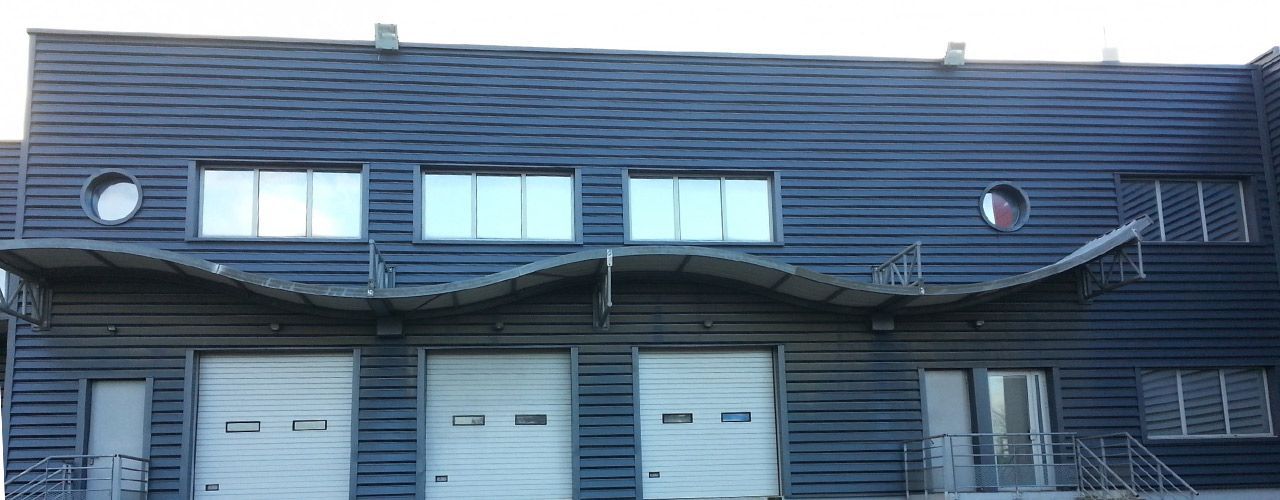 Un bâtiment gris foncé avec trois portes de garage, des fenêtres et un auvent incurvé.