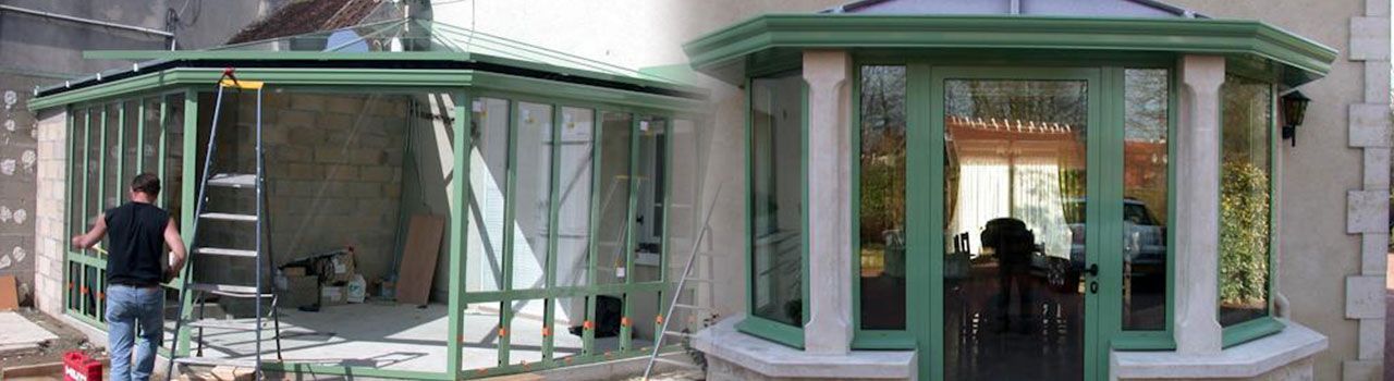 Une personne travaille sur une véranda à ossature de verre verte. Une partie est en construction.