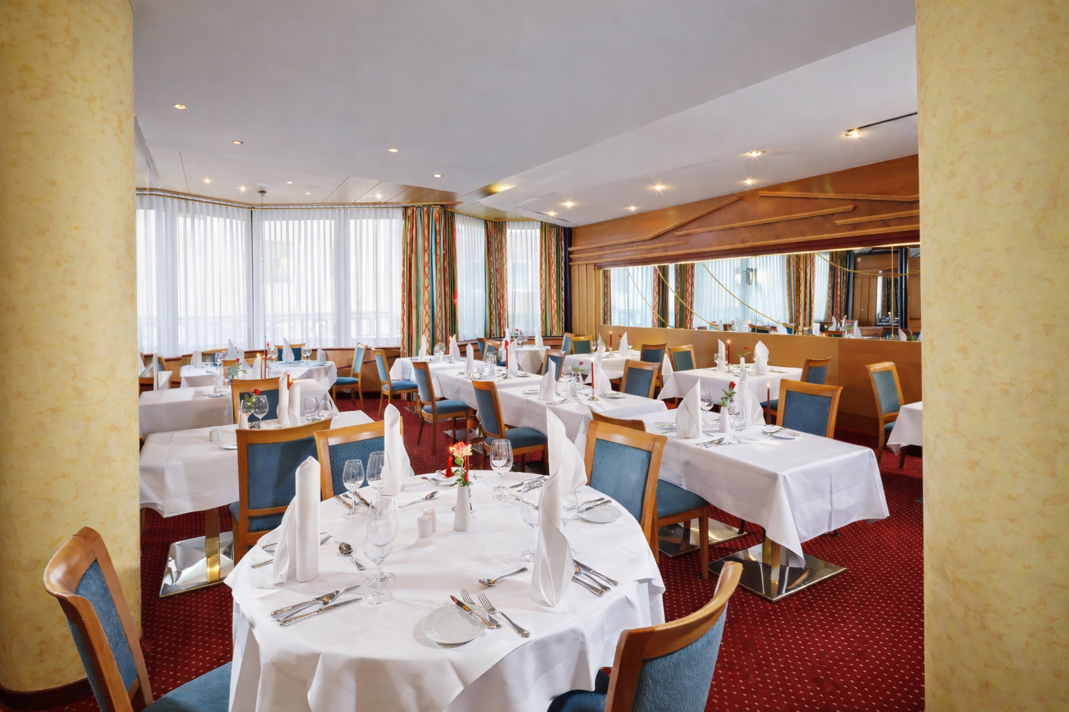 Leerer Speisesaal eines Restaurants mit weißen Tischdecken, rotem Teppich und blauen Stühlen
