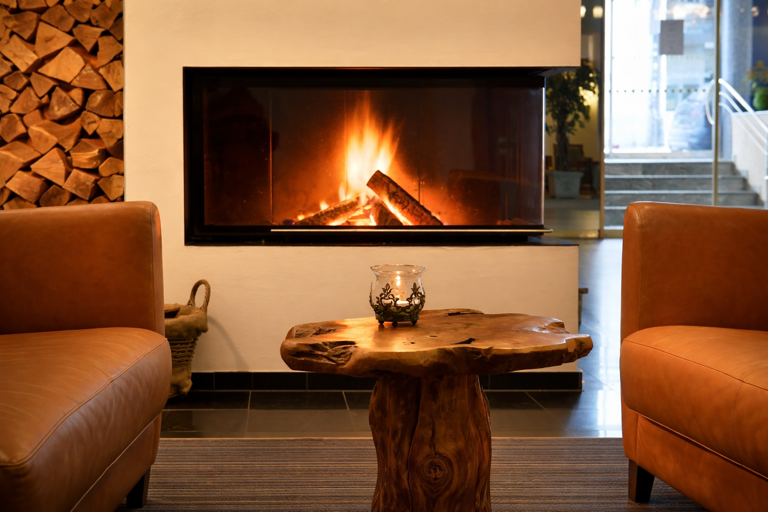 Modernes Wohnzimmer mit beleuchtetem Kamin, Couchtisch aus Holz und hellbraunen Sesseln.