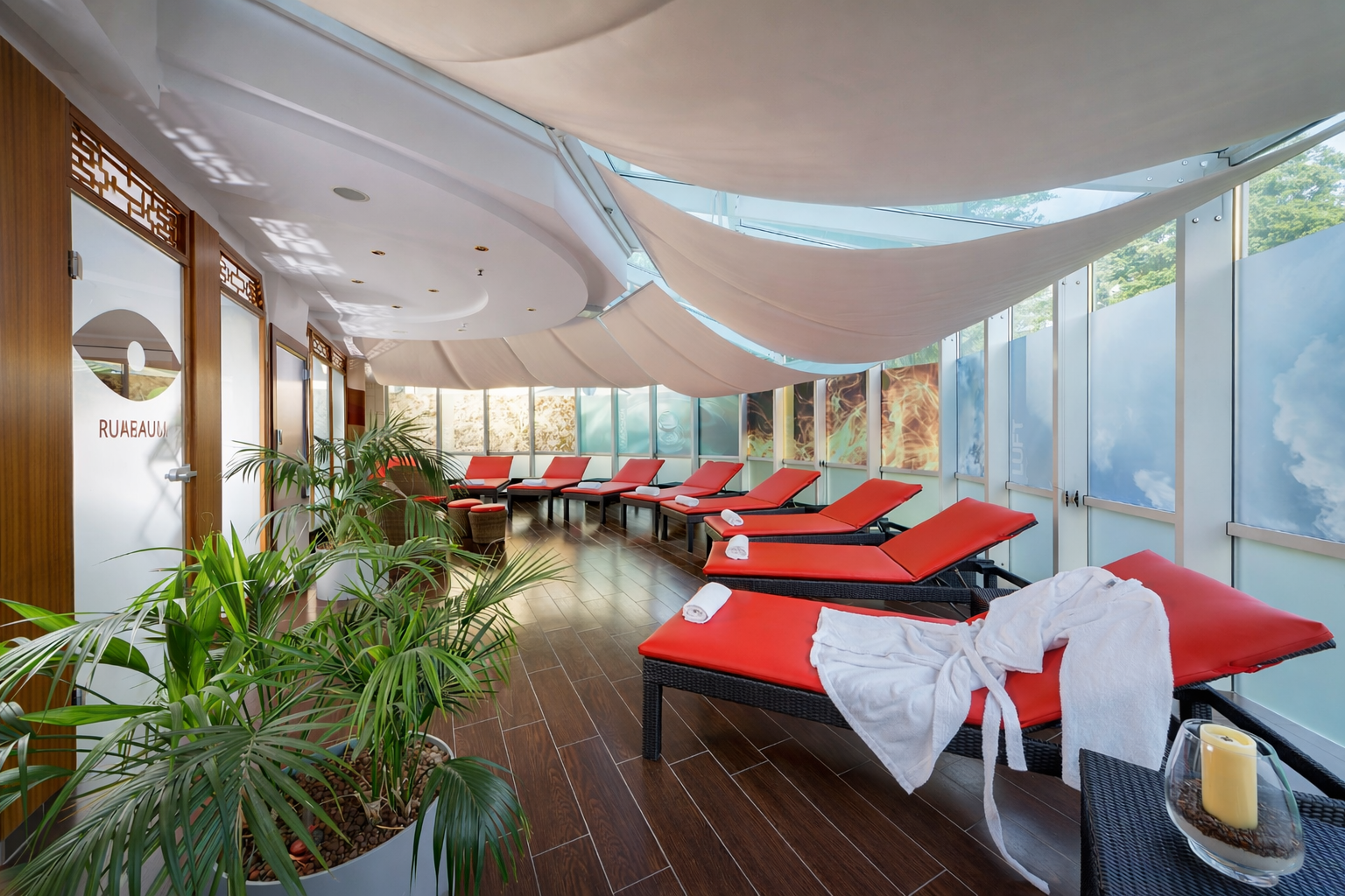 Moderne Spa-Lounge mit roten Liegesesseln, Holzböden und großen Fenstern mit Blick ins Grüne