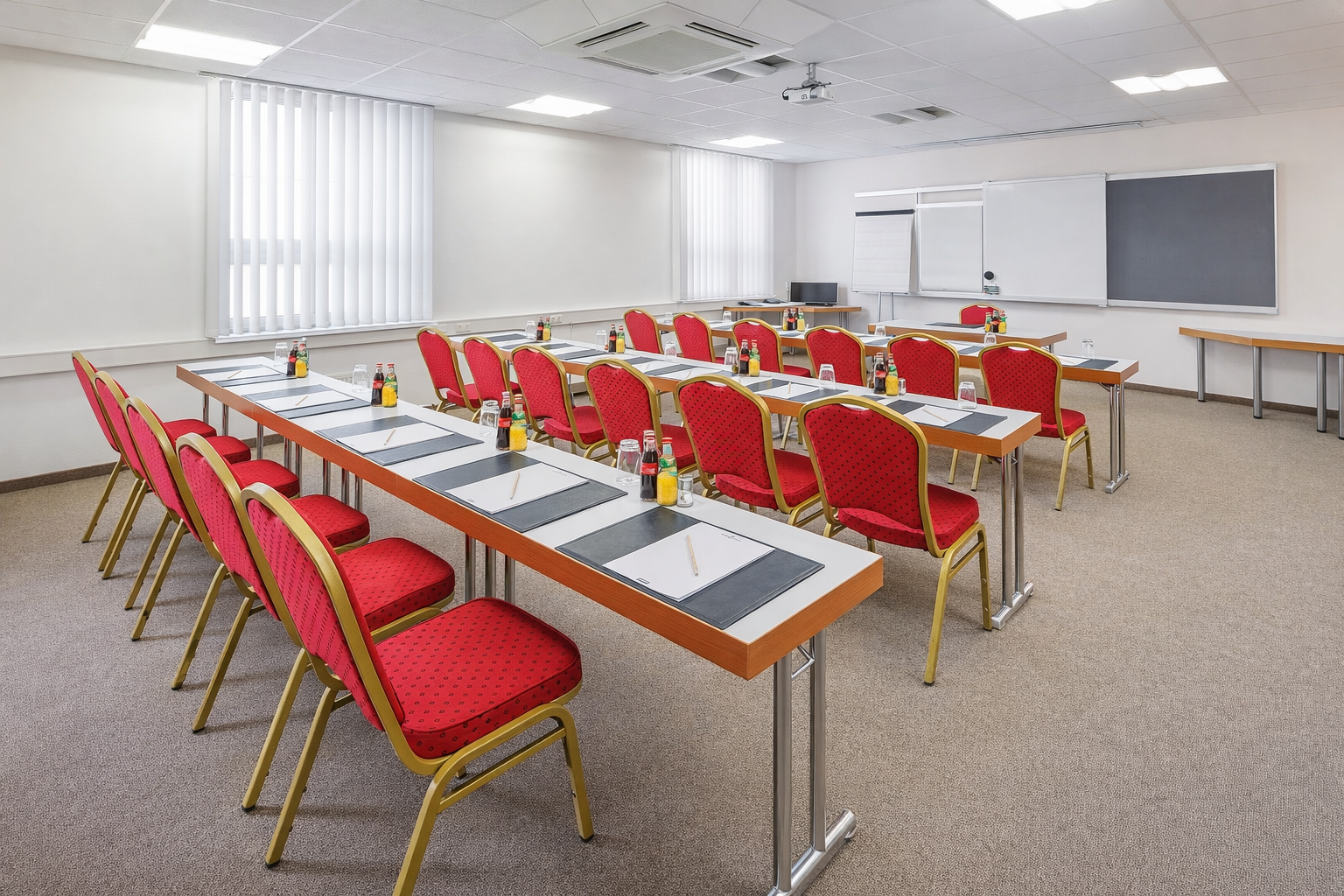Leeres Klassenzimmer mit roten Stühlen, langen Tischen und einer Tafel in einem hellen Besprechungsraum