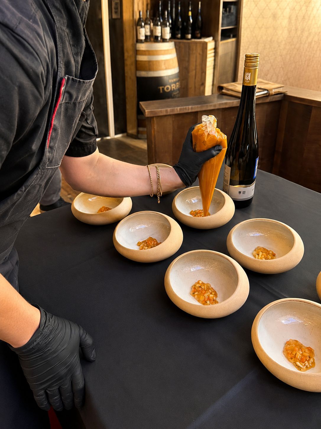 Ein Koch richtet in einer Restaurantküche kleine Vorspeisen auf weißen Schüsseln an einem schwarzen Tisch an.