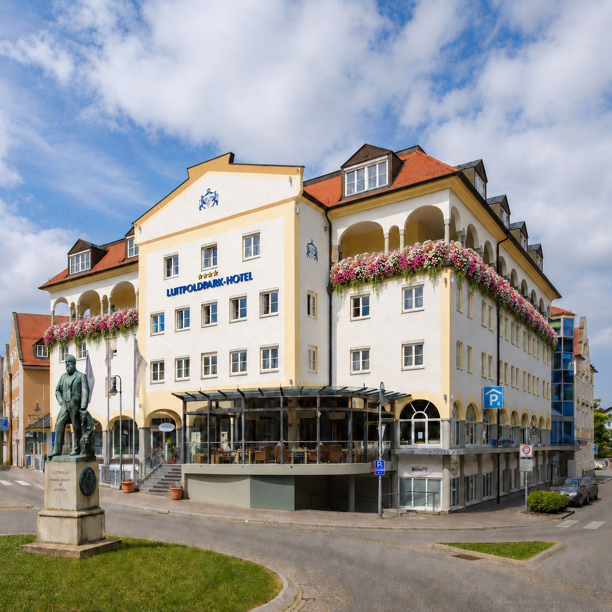 Historisches Hotelgebäude mit weißer Fassade, Blumenkästen und rotem Dach an einer sonnigen Straßenecke