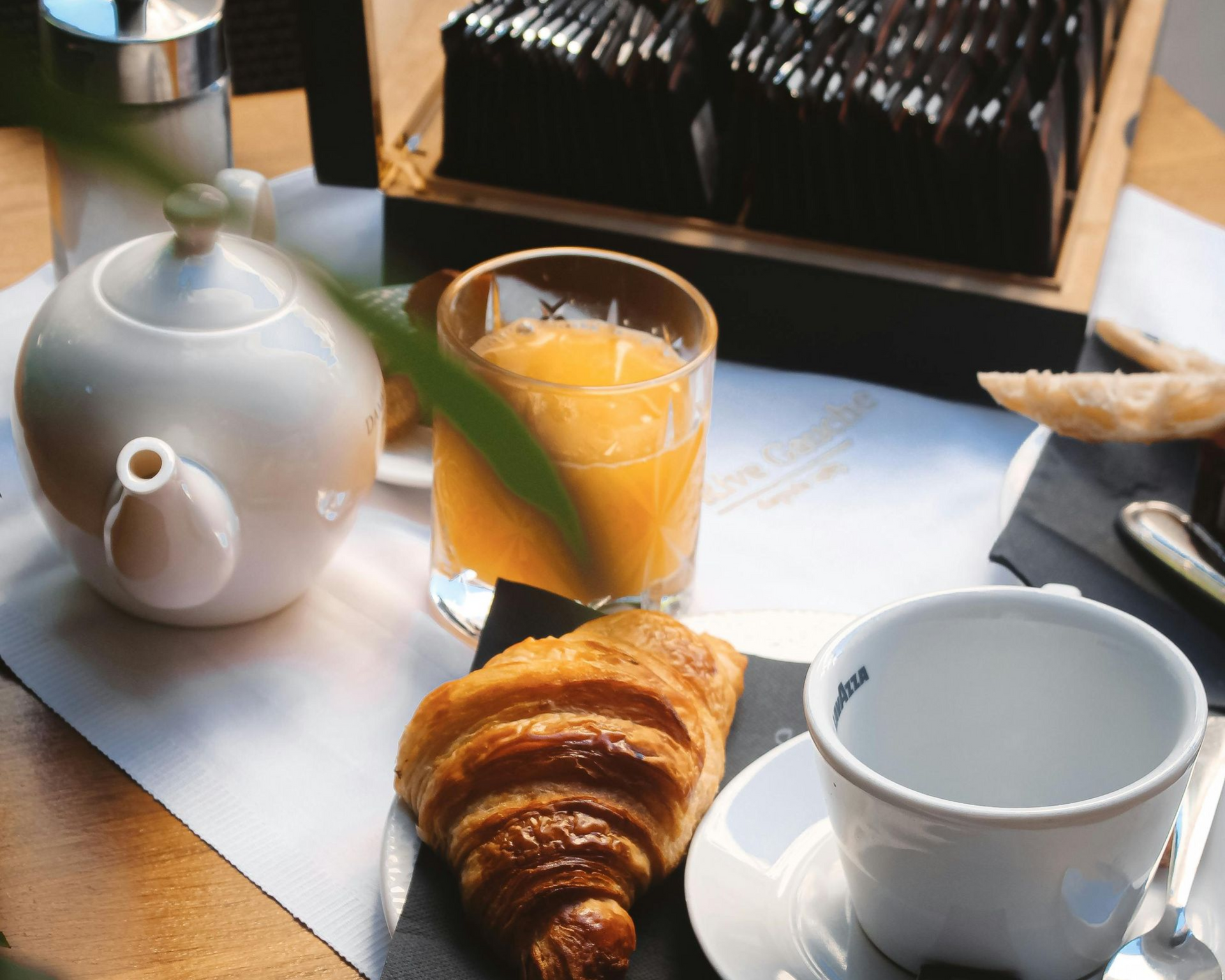 Teeservice, Orangensaft, Croissant und eine Tasse auf einem Tablett neben einer weißen Teekanne.