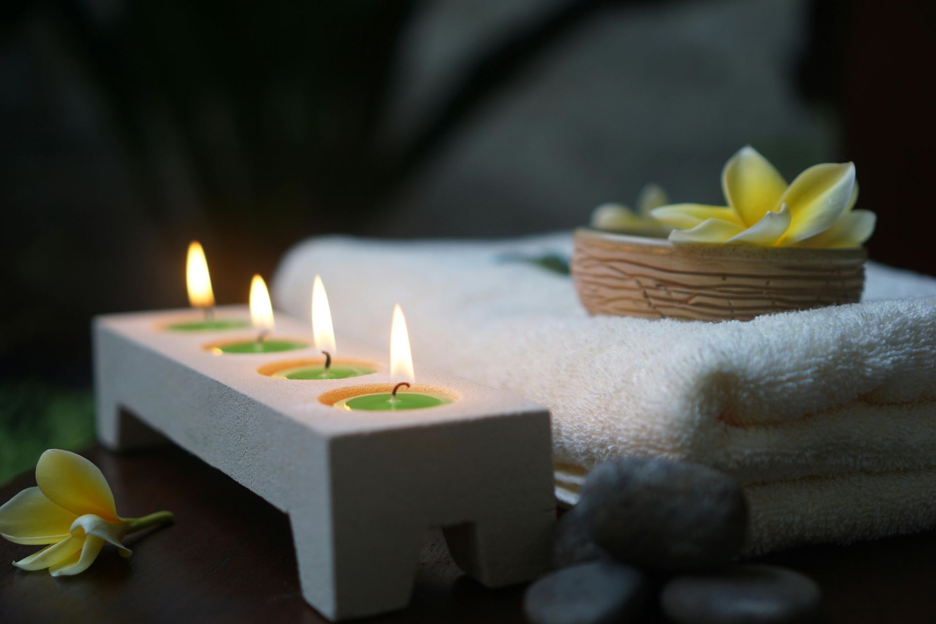 Spa-Kerzen und gelbe Blumen neben einem gefalteten weißen Handtuch und Steinen in einer ruhigen Umgebung