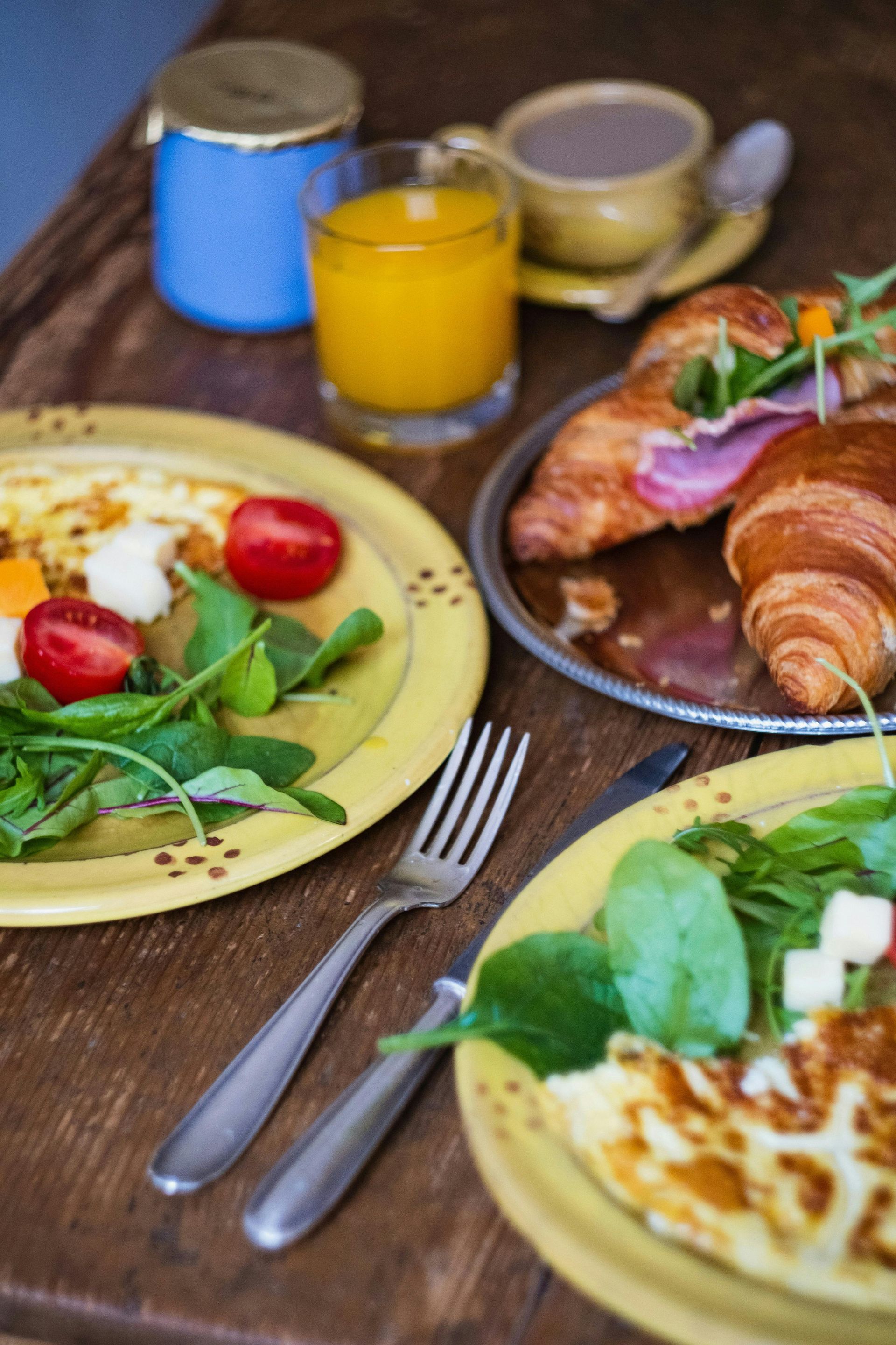 Frühstückstisch mit Gebäck, Obsttellern, Orangensaft, Kaffee und Gabeln auf einem Holztisch