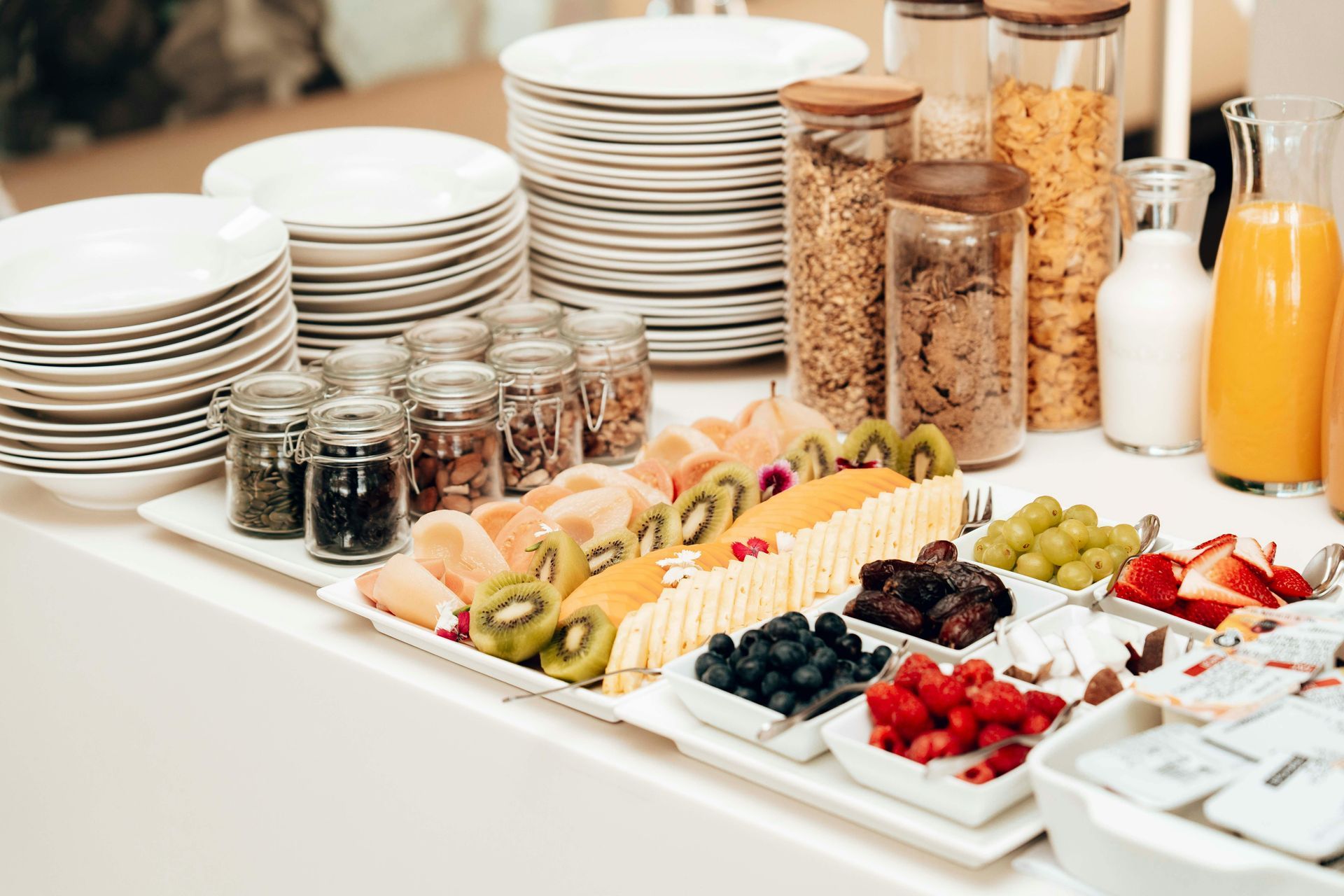 Frühstücksbuffet mit Tellern, Gläsern mit Müsli, Obst, Joghurt und Orangensaft