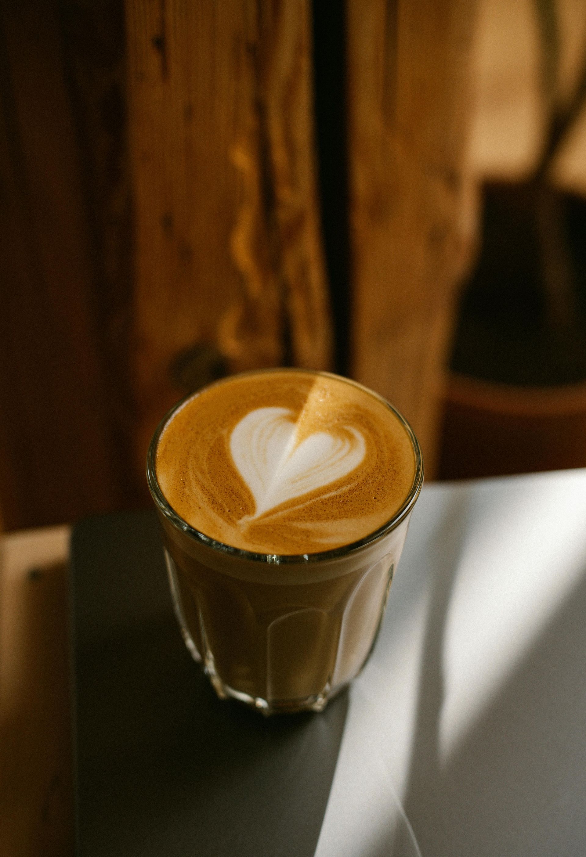 Ein Glas Latte mit herzförmigem Schaum auf einem dunklen Tisch in der Nähe eines Fensters