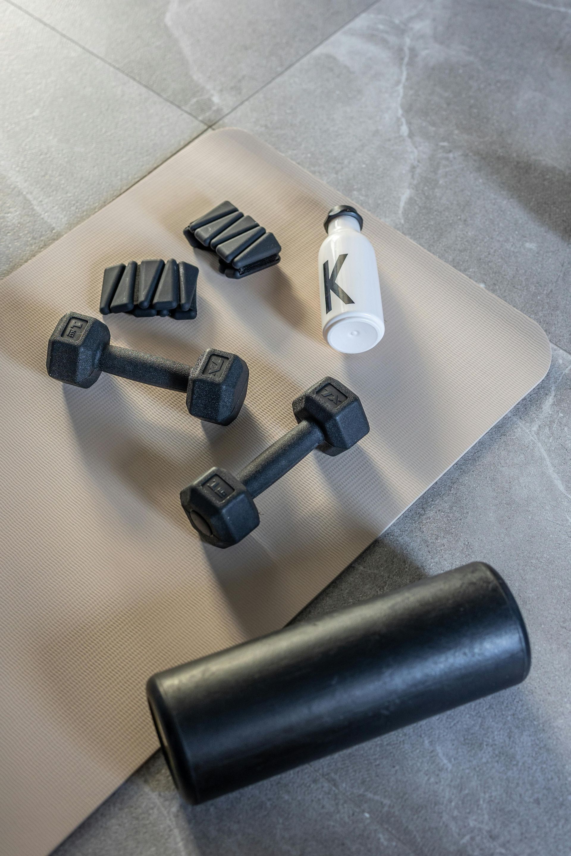 Yogamatte mit schwarzen Hanteln, Schaumstoffrolle, Widerstandsbändern und einer Wasserflasche auf dem Boden