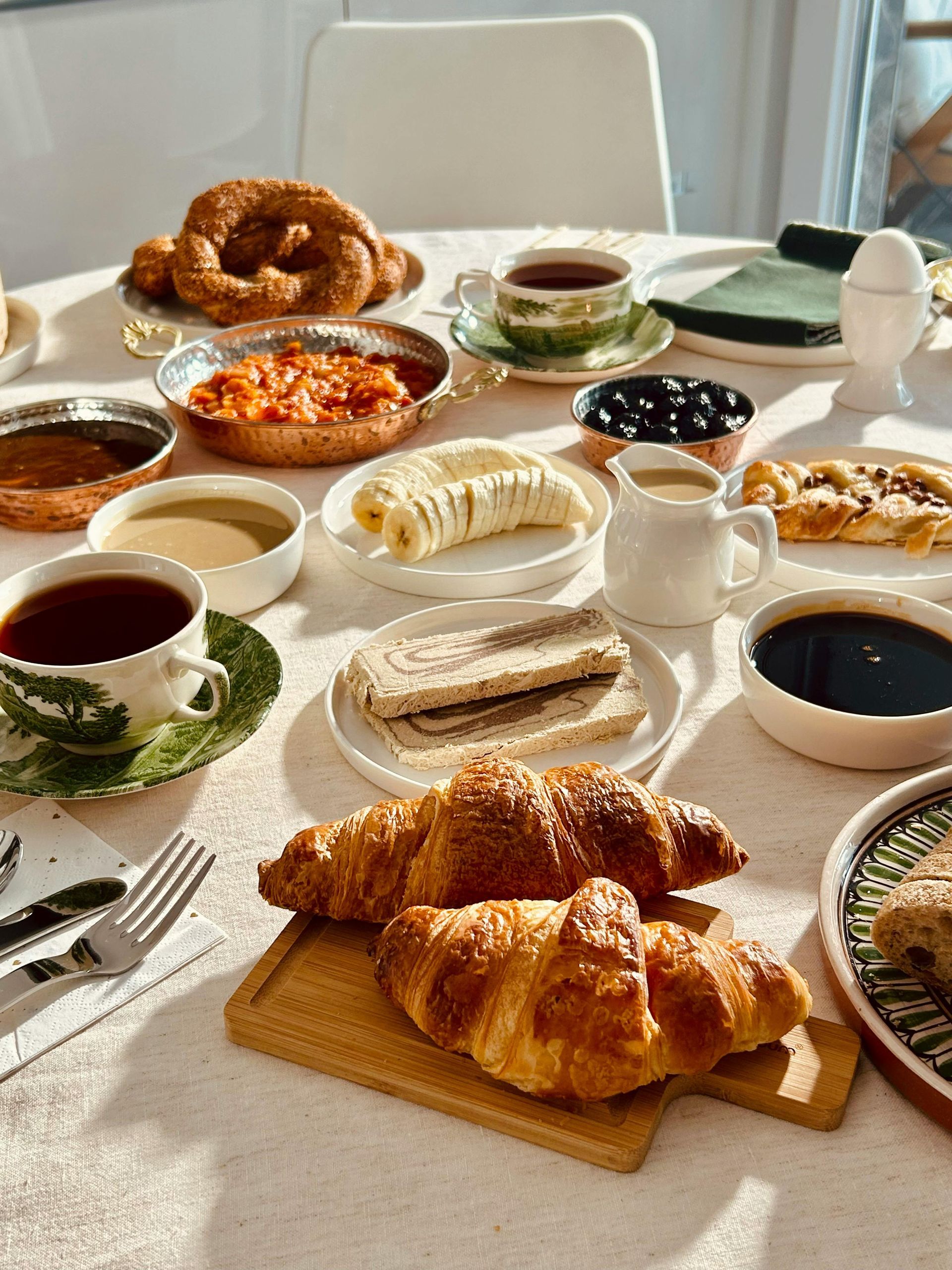 Ein reich gedeckter Frühstückstisch mit Croissants, Gebäck, Kaffee und Teetassen.
