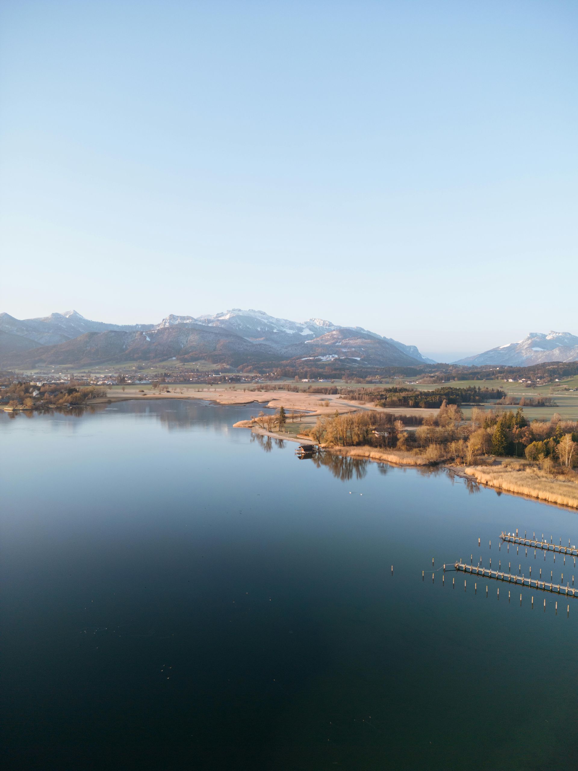 Ruhiger See neben trockenen Graslandschaften und fernen Bergen unter klarem, blauem Himmel