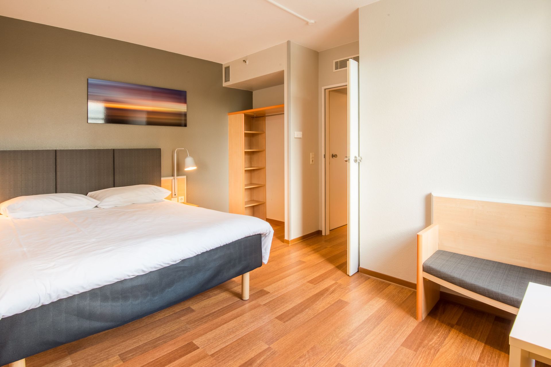 Modernes Schlafzimmer mit großem Bett, Holzboden und einer kleinen Bank an der Wand.