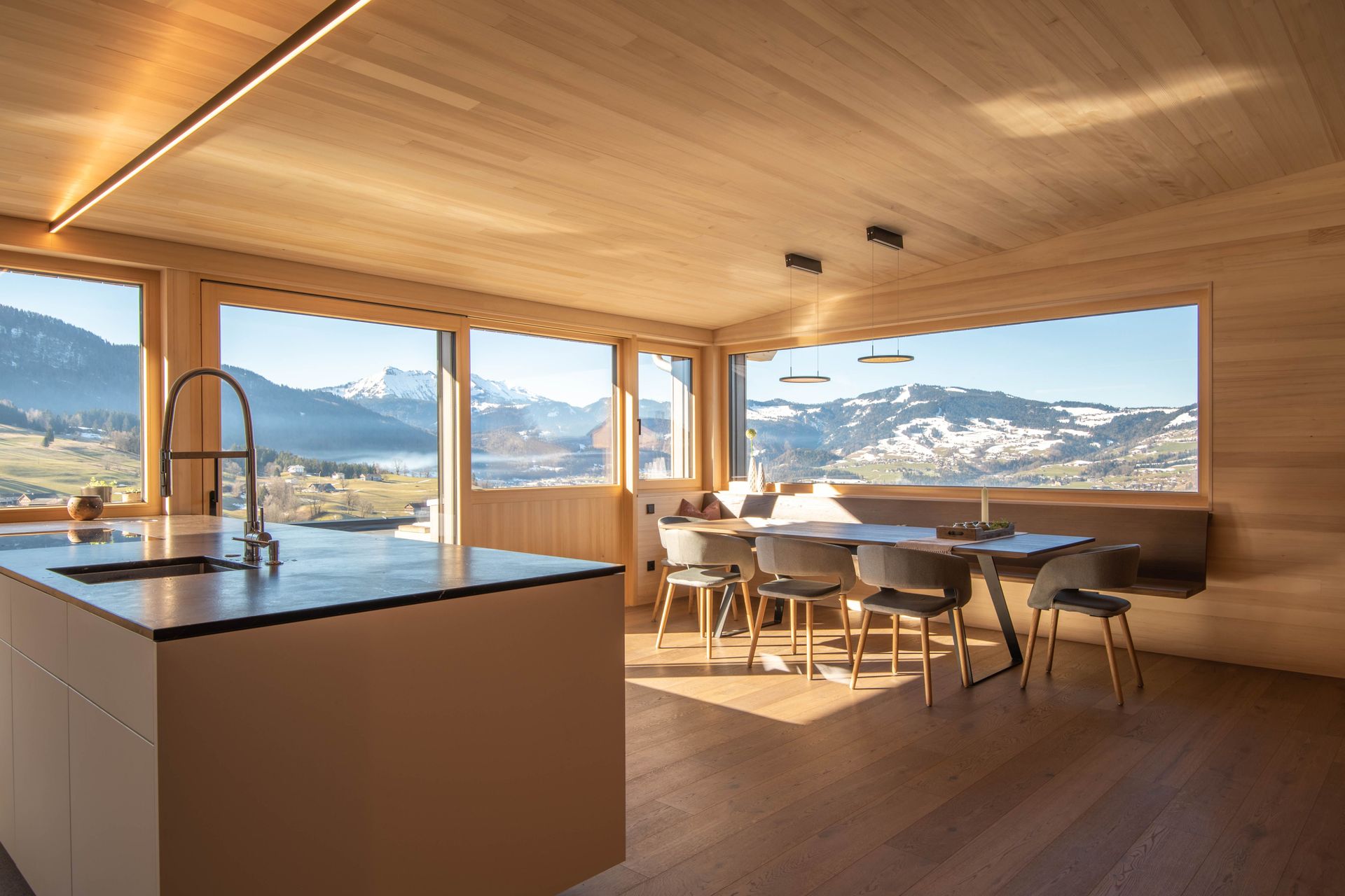 Moderne Küche und Essbereich mit Holzdecke, großen Fenstern und Blick auf den Bergsee