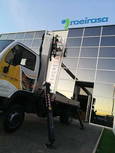 Un camión con una grúa acoplada está estacionado delante de un edificio.