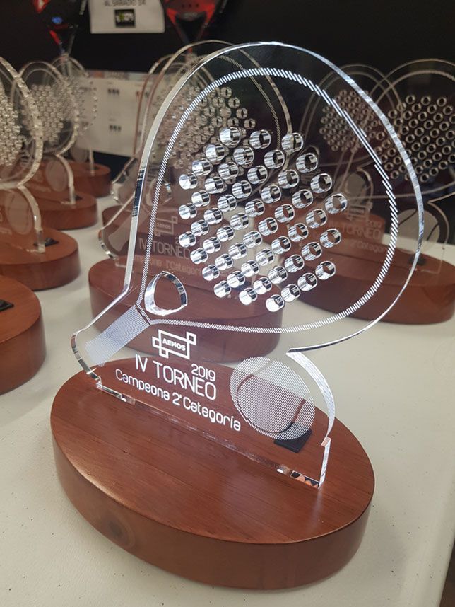 Un trofeo de acrílico transparente con una raqueta de tenis sobre una base de madera.