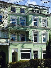 ein großes grünes Gebäude mit vielen Fenstern und Bäumen davor.