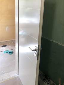 In einem Raum mit grüner Wand steht eine weiße Tür offen.