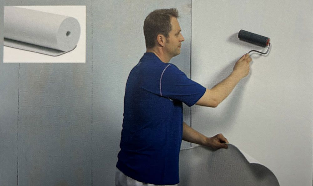 Ein Mann in einem blauen Hemd streicht mit einer Walze eine Wand