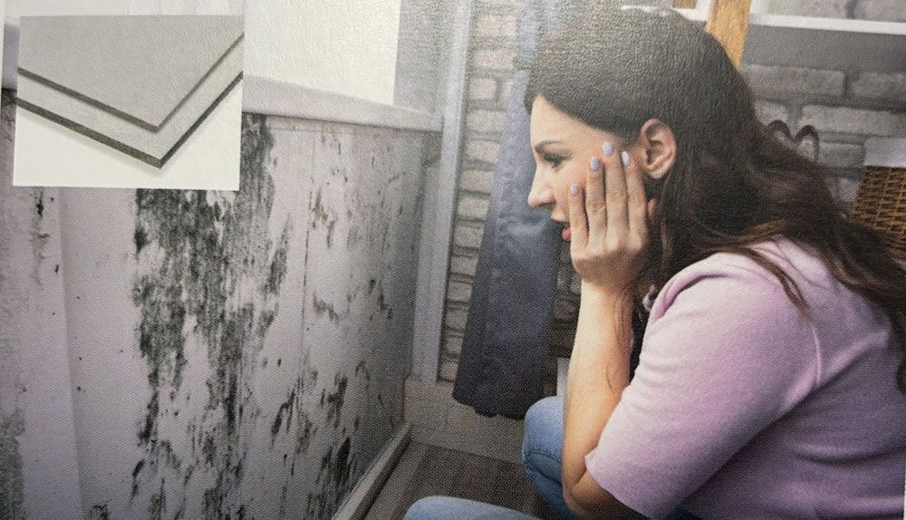 Eine Frau sitzt auf dem Boden und blickt auf eine schimmelige Wand.