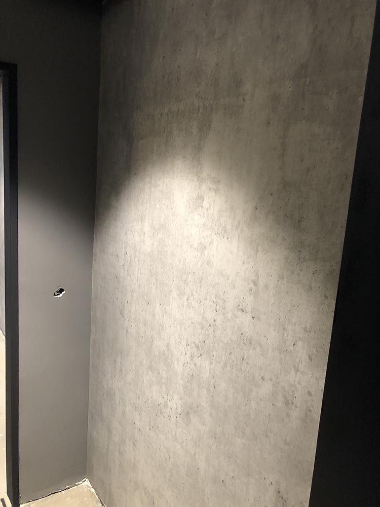 eine Ecke eines Raumes mit einer grauen Wand und einer schwarzen Tür.