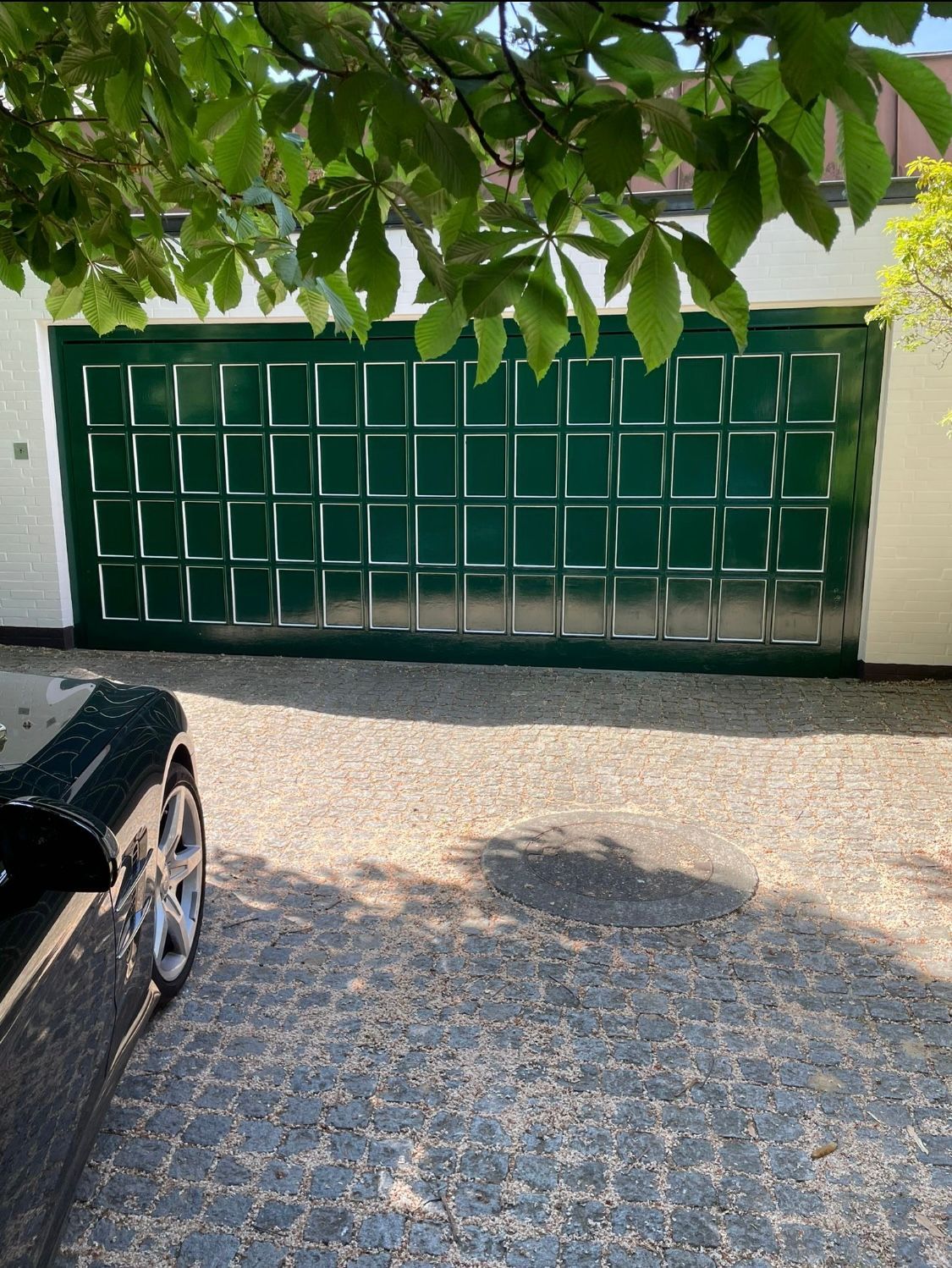 Ein schwarzes Auto parkt vor einem grünen Garagentor.
