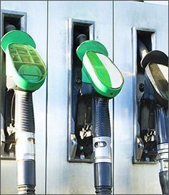 Tres boquillas de surtidor de combustible con mangos verdes y negros acopladas a una unidad de surtidor de gasolinera.