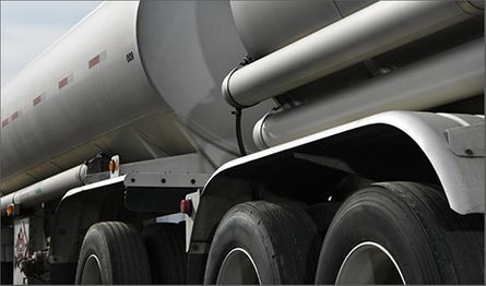 Vista de cerca del lateral, los neumáticos grandes y el chasis metálico de un remolque cisterna plateado.