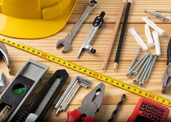 Un casco amarillo está sobre una mesa de madera rodeado de herramientas.