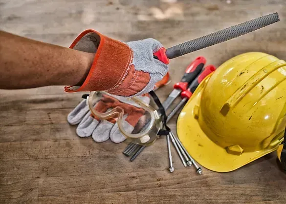Una persona que lleva guantes, gafas protectoras, casco y una lima.