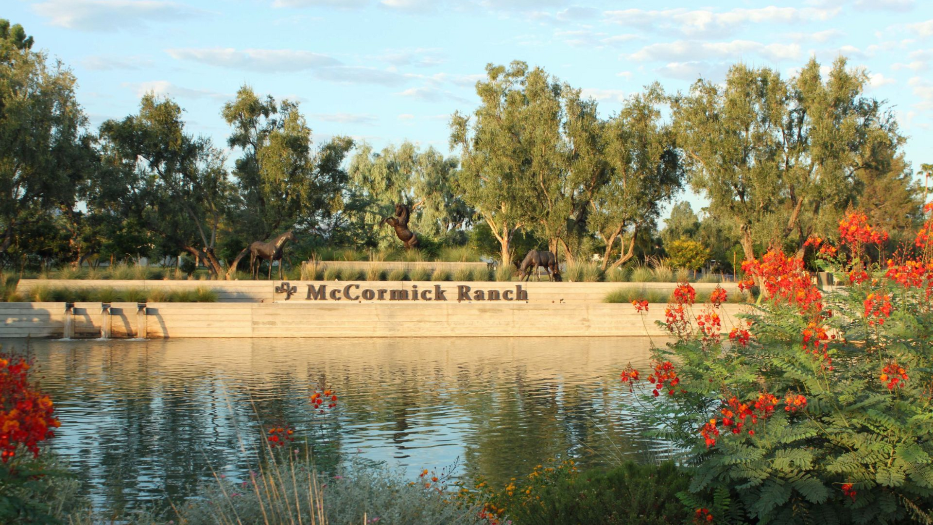 McCormick Ranch sign next to a reflective pond with trees and orange flowers in the foreground.