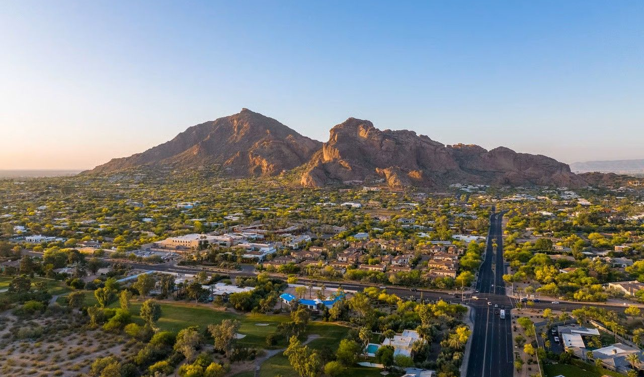 Mountain range overlooking a city with green trees and a road in Arizona at sunset.